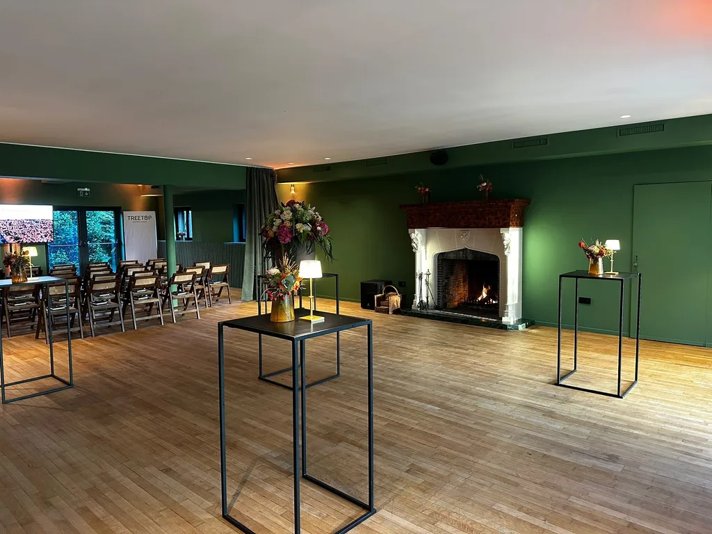 Evenementenzaal van Le Barbizon met brandende open haard, groene muren en bloemrijke statafels