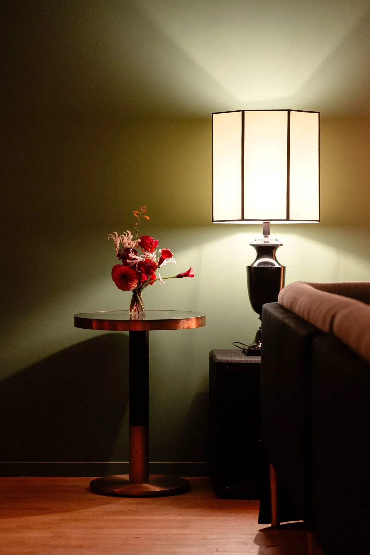 Lampe allumée et bouquet sur une table près du canapé du salon vert du Barbizon