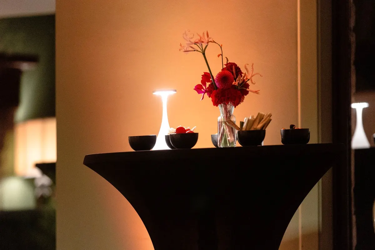 Hoge tafel met rood boeket en brandend lampje in warm amberlicht in de salon