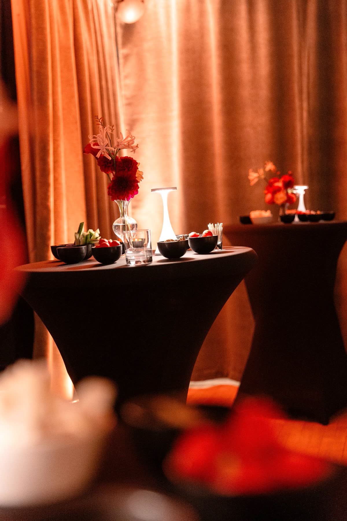 Statafel met zwart tafelkleed, rood boeket en hapjes in de salon van Le Barbizon, in warm amberlicht